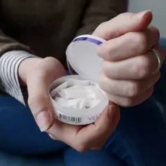 Händer som håller en dosa snus. En kvinna tar fram en prilla ur dosan.