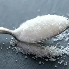 En sked med socker som innehåller onico socker. Sockerflingorna glittrar på den mörka ytan.