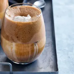 En glas med grekisk frappe, fylld med is och toppad med grädde.
