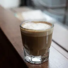 En perfekt cortado macchiato med krämigt skum, serverad i ett glas på en träyta.