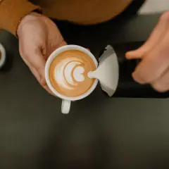 Barista häller mjölkskum i en kopp kaffe för att skapa lattekonst. Vad betyder latte? En kaffedryck med espresso och ångad mjölk.