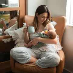 En mamma med en bebis i famnen dricker kaffe. Koffein amma är en konst.