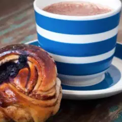 En blårandig kopp med kaffe och en kanelbulle med blåbär. Perfekt för en fika till jobbet.