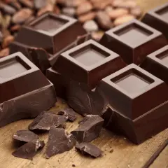 Mörk chokladbitar på träbord, med kakaobönor i bakgrunden. En härlig källa till kakao och koffein för en energikick.