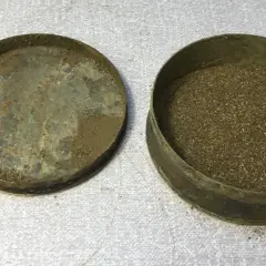 En gammal snusdosa med lock bredvid, fylld med utgånget snus.