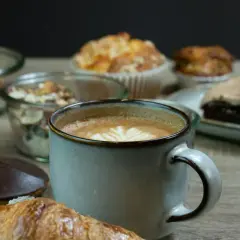 En kopp kaffe med lattekonst, en croissant och olika bakverk. En påminnelse om vart kommer kaffe ifrån och njutningen det ger.
