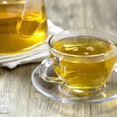 En kopp gyllene kamomillte, utan koffein, står på ett fat bredvid en tekanna.