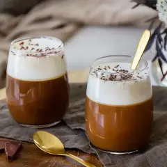 Två glas med kaffe drinkar med alkohol, toppade med grädde och chokladströssel. En gyllene sked vilar i det ena glaset.