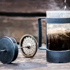 Varmt vatten hälls över kaffepulver i en presskaffe i kaffebryggare. Ånga stiger från den nybryggda drycken.