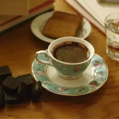En kopp mörkt, aromatiskt kaffe med garvsyra, bredvid mörk choklad och en bok. En perfekt stund för avkoppling.