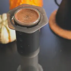 En kopp aeropress kaffe med en pumpa i bakgrunden.