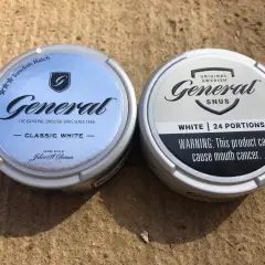Två dosor General snus, en Classic White och en White, ligger på en sandig yta.