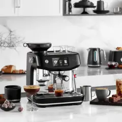 Snygg espressomaskin med inbyggd kvarn, som förbereder vanligt kaffe. Bredvid står godsaker och en kaffekopp.