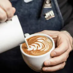 Barista skapar vacker latte art genom att hälla mjölk i en kaffekopp.