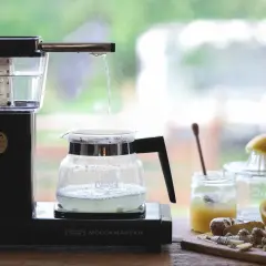 Vatten droppar från en kaffebryggare ner i en glaskanna, redo att brygga te. Ingredienser som citron och ingefära syns i bakgrunden.