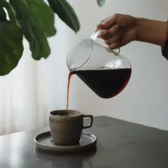 En hand häller upp mörkt kaffe ur en glaskanna i en mugg. Kaffet innehåller njutning och energi.