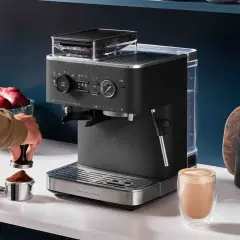 En person förbereder espresso i en kaffebryggare. En färdigbryggd latte står bredvid.