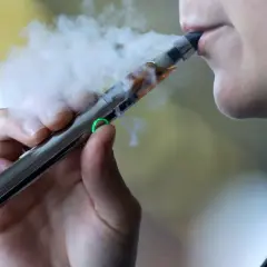 En person tar ett bloss på en e-cigarett inomhus, med ånga som syns tydligt.