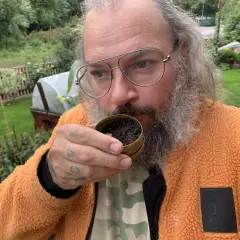 Man med glasögon och skägg luktar på en dosa snus, kanske för att avgöra om det är dags att göra ett nytt snus recept.