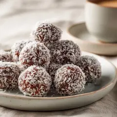En hög med chokladbollar täckta av kokosflingor, redo att avnjutas med en kopp kaffe.