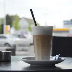 En hög latte macchiato med skummig mjölk och en sked, redo att avnjutas vid ett cafébord utomhus.