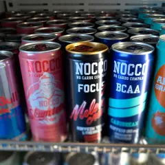 En rad NOCCO-burkar, inklusive "Skumtomte" och "Focus Melon Crush", samt Red Bull och Celsius. Frågan "hur mycket koffein i NOCCO" kan besvaras genom att läsa på burkarna.