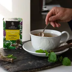 En hand rör om i en kopp te. Bredvid står en ask med Skandinavisk Twist Lakritstäppa, som ger te smak.