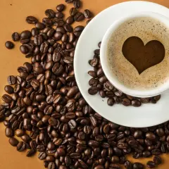 En kopp kaffe med ett hjärta i skummet, omgiven av kaffebönor. En visuell förklaring till hur fungerar koffein.