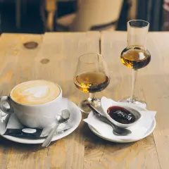 En kopp kaffe med vitt hjärta på skummet, bredvid två glas med bärnstensfärgad dryck och en skål med sylt. En perfekt kombination för en stunds njutning.