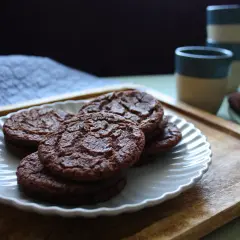 Chokladkakor på en vit tallrik, redo som en snabb kaka till kaffet. Bredvid står staplade muggar.