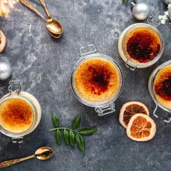 Fyra krämiga creme brulee i glasburkar, toppade med karamelliserat socker. En festlig dukning med torkad apelsin, julgranskulor och gnistrande stjärntändare.