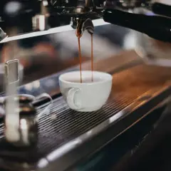 Espresso rinner ner i en vit kopp. En liten mjölkkanna står bredvid, redo för att skapa perfekt kaffeskum.