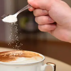 En hand häller socker från en sked ner i en kopp kaffe. Kanske är det salt i kaffet istället för socker?
