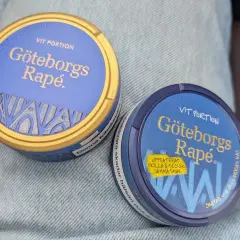 Två dosor Göteborgs Rapé, en med guldig kant, ligger på jeans. Perfekt för dig som vill ha snus som inte rinner.