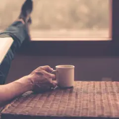 En person läser en bok med en kopp kaffe, njuter av stunden och funderar över kaffe ursprung.