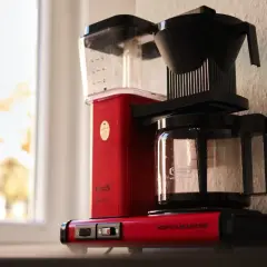 Röd Moccamaster kaffebryggare vid fönstret, redo att brygga en god kopp kaffe.