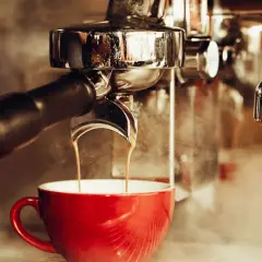 En röd kopp fylls med rykande espresso från en maskin. En klassisk italiensk kaffeupplevelse.