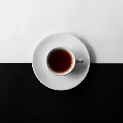 En vit kopp med mörkt kaffe står på en vit tefat, delar en yta som är uppdelad i svart och vitt. Kan kaffe bli gammalt?