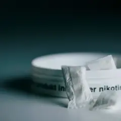 En dosa snus, ett populärt naswar i Sverige, med några påsar framför.