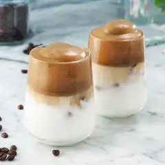 Två glas med krämiga kaffedrinkar med rom, toppade med fluffigt skum. Kaffebönor sprider sig på bordet.