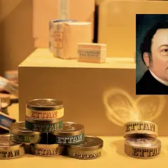 Porträtt av en man bredvid staplar av snusdosor med texten "Ettan". En historisk fråga är vem uppfann snus.