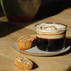 En lyxig kaffe creme med vispad grädde och kanel, serverad med mandelkakor på en träyta.