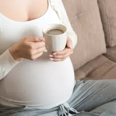 En gravid kvinna sitter på en soffa och håller en mugg med kaffe.