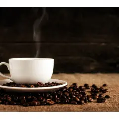 En vit kaffekopp i dl, omgiven av rostade kaffebönor, med ånga som stiger upp.