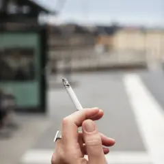 En kvinna röker en cigarett vid en busshållplats. Bilden kan illustrera prisutveckling cigaretter.