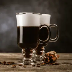 Två glas med krämig cappuccino, kaffebönor och kanelstänger. Perfekt för ett mysigt cappuccino recept.