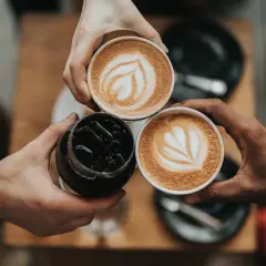 Tre händer håller varsin kopp med kaffe. Två koppar har vacker latte art, en är en kaffe macchiato.