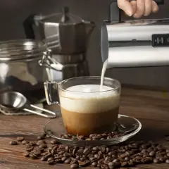 En hand häller mjölkskum i en kaffekopp, redo för ett perfekt kaffe recept. Kaffebönor sprider sig över träbordet.