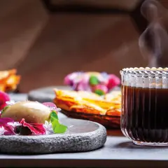 En ångande kopp kaffe glass serveras med en elegant dessert.