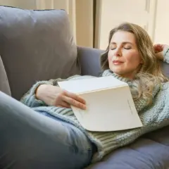 Kvinna vilar på soffan med en bok i famnen, drömmer om hur lång ska en powernap vara för maximal återhämtning.
